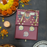 Decorative gift box with maroon and gold design, surrounded by flowers, candles, and food items on a dark surface.