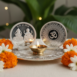 Decorative setting with silver coasters featuring engraved designs, a lit candle, and marigold flowers on a light surface.