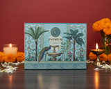 Decorative box with palm tree design on a table with candles and flowers against a red background