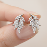 Silver leaf-shaped earrings held between fingers against a neutral background