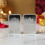 Two silver bars with embossed designs on a reflective surface with a blurred decorative background.