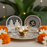 Decorative setting with silver coasters featuring engraved designs, a lit candle, and marigold flowers on a light surface.