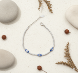 Bracelet with blue evil eye beads on a sandy surface with stones and plants.