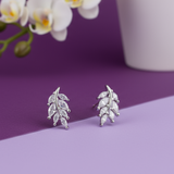 Silver leaf earrings on a purple surface with a white vase and orchid in the background