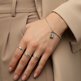 Hand wearing multiple silver rings and a bracelet on a neutral background