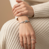 Close-up of a person's hand wearing a silver bracelet and ring on a beige background