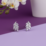Silver leaf earrings on a purple surface with a white vase and orchid in the background
