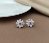 Flower-shaped earrings with red gemstones on a brown surface